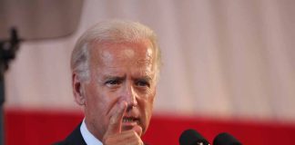 Man speaking at a podium, pointing finger upwards.