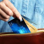 Hand holding credit cards over a brown purse.