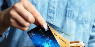 Hand holding credit cards over a brown purse.