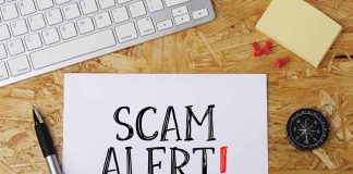 Scam alert message on a wooden desk.