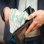 Hand holding wallet with hundred dollar bills