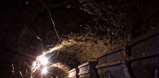 Dimly lit mine shaft with rail carts and tracks.
