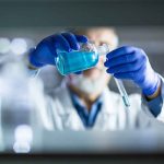 Scientist pouring blue liquid into test tube.