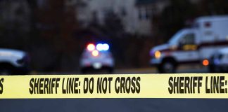 Sheriff line tape with emergency vehicles in background.