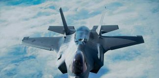 Jet flying above clouds, viewed from front.