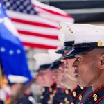 Marines in uniform standing in line, American flags displayed.