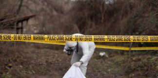 Crime scene investigator examining area with police tape