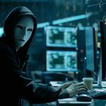 Person wearing mask and hoodie at computer desk