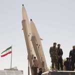 Military personnel beside missiles and Iranian flag