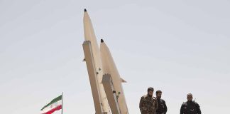 Military personnel beside missiles and Iranian flag