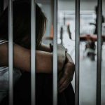 Person sitting behind bars with arms wrapped around knees