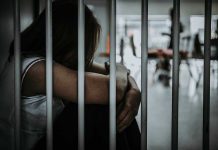 Person sitting behind bars with arms wrapped around knees