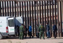People near border fence with border patrol van
