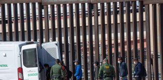 People near border fence with border patrol van