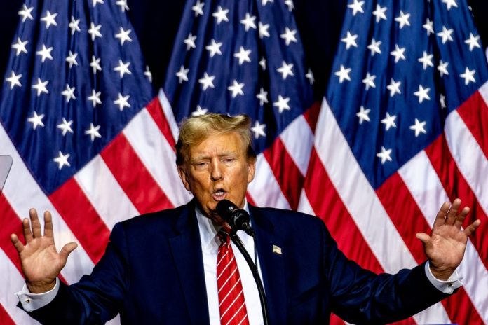 2551951931 featured image Man speaking on stage with multiple American flags
