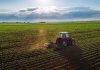 Tractor plowing a vast green field at sunset