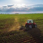 Tractor plowing a vast green field at sunset