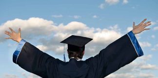 Graduate in cap and gown celebrates under cloudy sky