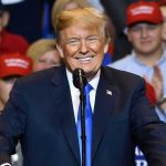 Man in suit speaking at rally with red hats
