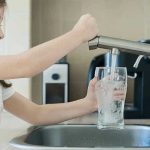 Girl filling glass with water from kitchen faucet