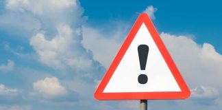 Warning sign with exclamation mark against cloudy sky