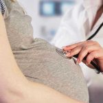 Doctor uses stethoscope on pregnant woman's belly