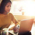 Woman using a laptop while holding a mug