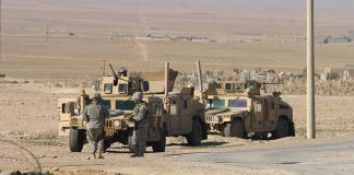 Soldiers standing near armored vehicles in desert terrain