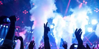 Crowd at a concert with hands raised and smoke effects in the background