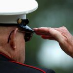 A veteran in military uniform saluting with a hand raised