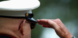 A veteran in military uniform saluting with a hand raised