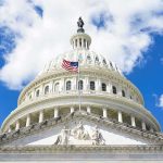 The US Capitol building with an American flag flying in front against a blue sky
