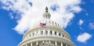The US Capitol building with an American flag flying in front against a blue sky