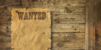 A vintage wanted poster pinned to a wooden wall