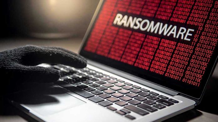 Gloved hand on laptop with ransomware screen.