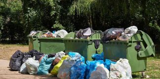 Overflowing garbage bins with bags on the ground.