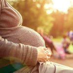 Pregnant woman sitting on a bench in a park during sunset