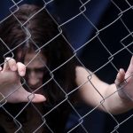 Four Adults Found Trapped—Police Stunned by Discovery A person with long dark hair reaching through a metal fence, expressing distress
