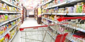 A shopping cart in a grocery store aisle filled with colorful products