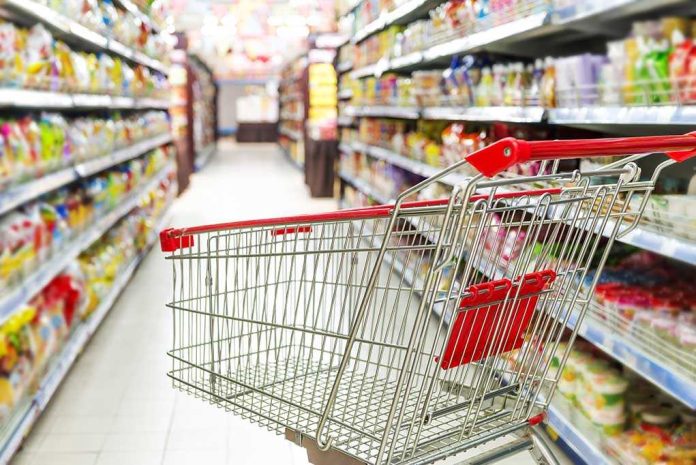 A shopping cart in a grocery store aisle filled with colorful products