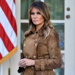 Stolen Kids RETURNED—Melania’s Wild Power Play! Woman in brown coat beside American flag.