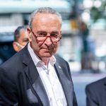 Shutdown Standoff –Trump TORCHES Schumer’s Leadership Man in suit and red glasses standing outside.