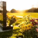 Sunlit cemetery with flowers on headstone.