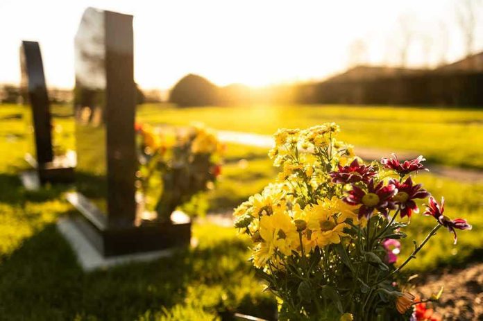 Sunlit cemetery with flowers on headstone.