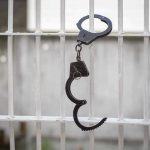 Prison Guard MURDERS Handcuffed Inmate – BRUTALITY Handcuffs hanging on white metal bars.