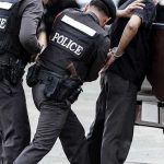 Police officers arresting a handcuffed person.