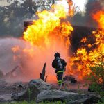 Firefighter battling a large fire with water spray
