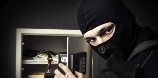 A masked burglar holding a gun while attempting to open a safe