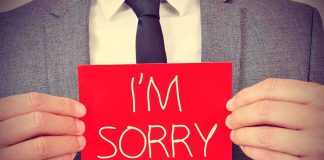 A man in a suit holding a red sign that says IM SORRY