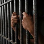 Hands gripping prison cell bars tightly.